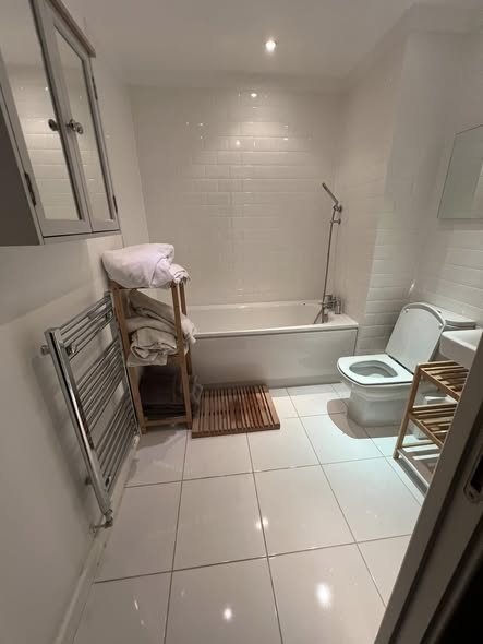 Finished bathroom with a bath, toilet, towel rail and clean white tiles