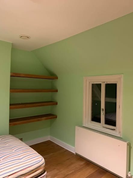Bedroom painted sage green with oak floating shelves
