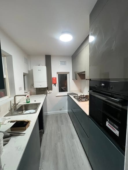 Galley kitchen with white upper units, grey lower units and a black oven
