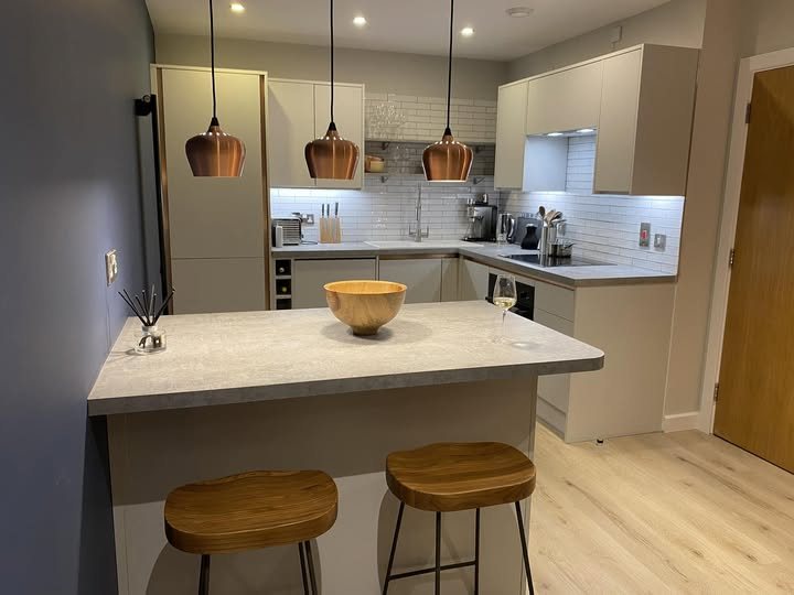 White fitted kitchen with an island, copper pendant lights and a wood floor