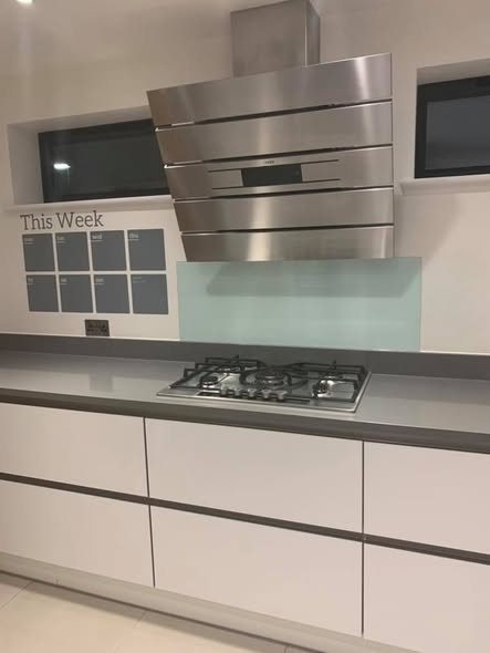 Fitted kitchen with a stainless steel hood, glass splashback and gas hob